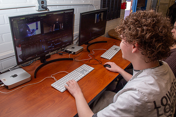 A teen boy with curly brown hair edits a video on a computer