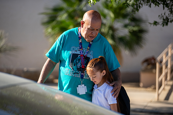A man in an aqua shirt hugs a young girl in a white polo