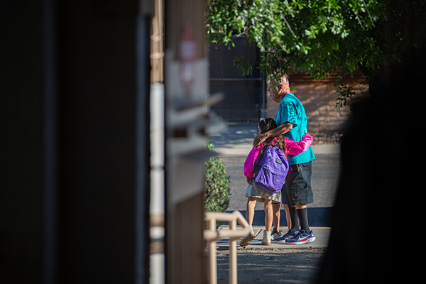 A man in an aqua shirt hugs a young girl in a pink jacket and purple backpack