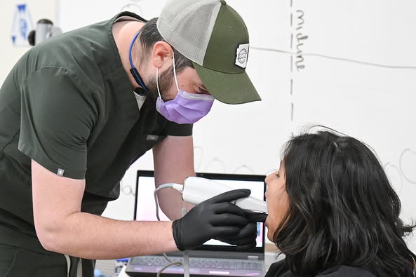A man wearing a purple mask performs a dental scan on a student