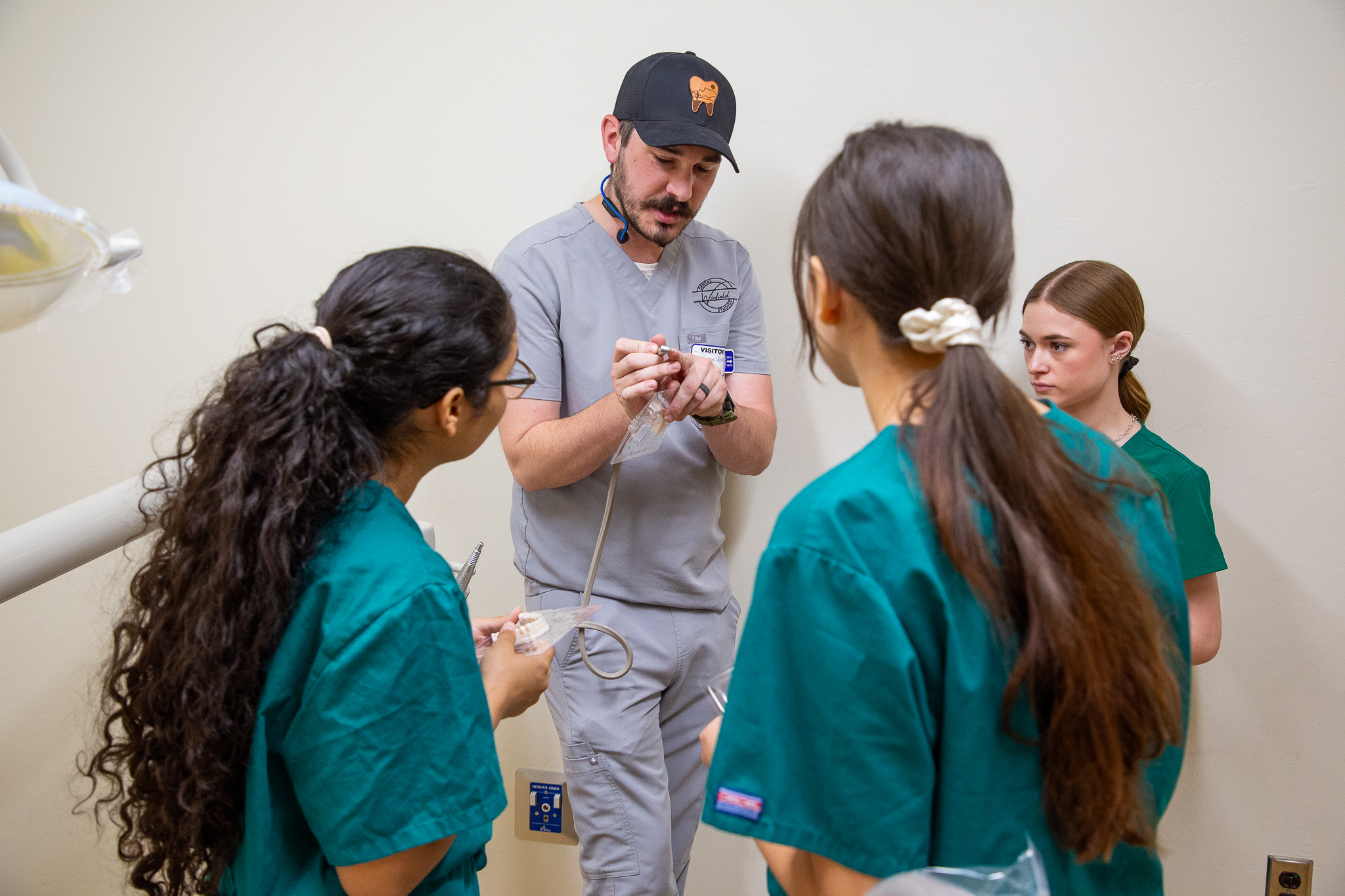 A man in scrubs demonstrates a tool to dental students