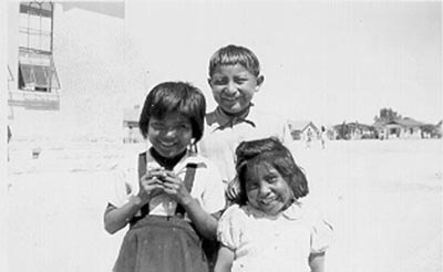 Three young students stand outside a school in the early days of TUSD.